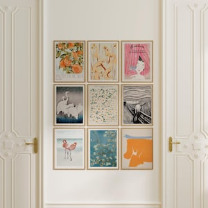 May include: Nine framed art prints with various designs, including citrus fruits, floral patterns, and abstract art. The prints are displayed on a white wall between two white doors with gold hardware. The prints are in wooden frames.