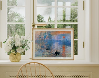 May include: A framed painting of a foggy seascape with a red sun setting over the water. The painting is in a light wood frame and is hanging on a white wall.