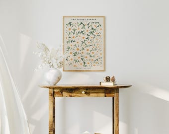 May include: A framed print of a floral design with white flowers and green leaves. The print has the text "The Secret Garden" and "Frances Hodgson Burnett" in black text. The print is hanging on a white wall above a wooden console table.