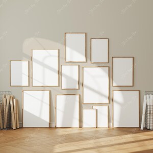 May include: A collection of blank picture frames with wooden borders, arranged on a beige wall. The frames vary in size and shape, creating a gallery wall effect. The floor is made of wooden planks.