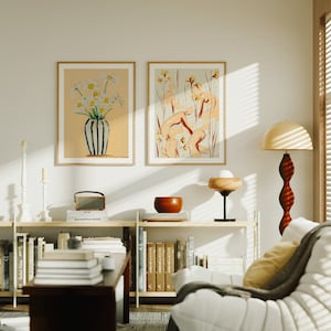 Op de afbeelding: Een woonkamer interieur met een witte bank, een houten boekenkast met boeken, twee ingelijste bloemendrukken, een houten lamp met een witte kap en een houten bijzettafel met een kom en een radio.