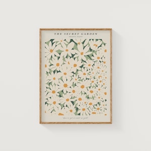 May include: A framed print with a white background featuring a floral pattern of white Shasta daisies with yellow centers on a green background. The text "THE SECRET GARDEN" and "SHASTA DAISY" is at the top of the print. The text "You've got a heart of gold." is at the bottom of the print.