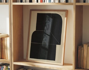 May include: A framed abstract art print featuring a black geometric design on a beige background. The artwork is displayed on a wooden bookshelf filled with books. The frame is a light brown color.