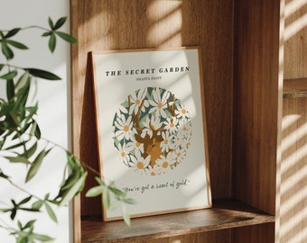 May include: A framed print with a white background and a circle of white flowers with a deer in the center. The text "THE SECRET GARDEN" and "SHAISTA DAISY" is at the top of the print. The text "You've got a heart of gold." is at the bottom of the print.