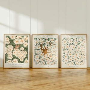 Op de afbeelding: Drie ingelijste prints met witte bloemen en groene bladeren. De bovenste print toont een hert, de middelste print toont een eekhoorn en de onderste print toont een vogel. Elke print heeft de tekst "The Secret Garden" en "Frances Hodgson Burnett" bovenaan.