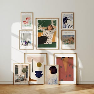 Peut inclure: Plusieurs tirages d'art encadrés sont affichés sur un mur blanc. Les impressions présentent divers styles, notamment des motifs abstraits, des portraits et des paysages. Certaines impressions comportent du texte, comme "OHARA KOSON" et "PIERRE-AUGUSTE RENOIR". Les cadres sont de couleur marron chaud.
