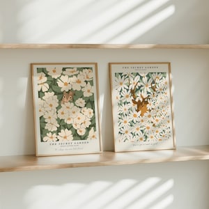 Puede incluir: Dos impresiones enmarcadas de ilustraciones florales con el texto "The Secret Garden" y citas del libro. La primera impresión presenta una ardilla escondida en un campo de flores blancas con hojas verdes. La segunda impresión presenta un ciervo escondido en un campo de flores blancas con hojas verdes.