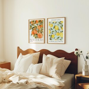 May include: Two framed watercolor prints of fruit on a white wall above a bed with a wooden headboard. The print on the left features oranges and the text "FRUTTI DI SICILIA". The print on the right features lemons and the text "POSITANO ALBERO DI LIMONE".
