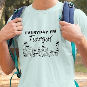 May include: A light blue t-shirt with the text "EVERYDAY I'M Foragin'" and a graphic of mushrooms and leaves.