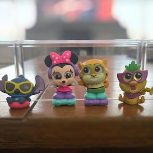 May include: A collection of colorful Disney character figurines, including a dog, Stitch, Minnie Mouse, a tiger, a bird, and a black cat. Each figure is uniquely designed with vibrant colors and details, displayed on a wooden surface.