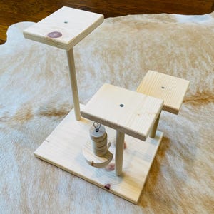 May include: A wooden toy for small animals with multiple platforms and a hanging toy. The toy is made of natural wood and has a simple design.