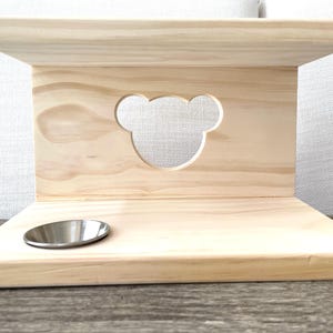 May include: A wooden pet feeder with a bear-shaped cutout and a metal bowl. The feeder is made of light wood and has a natural finish.