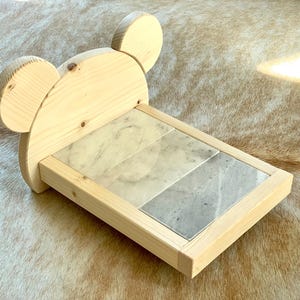 May include: A wooden mouse-shaped shelf with a rectangular base. The shelf features a light-colored wood frame and a marble tile insert. The mouse ears are rounded and add a playful touch to the design.