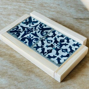 May include: A square wooden coaster set with four ceramic tiles. The tiles feature a white background with a dark blue floral pattern. The coaster is made of light-colored wood.