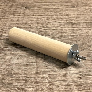 May include: A light-colored wooden perch for birds, cylindrical in shape, with a metal washer and bolt for attachment. The perch is approximately 6 inches long and 1 inch in diameter.