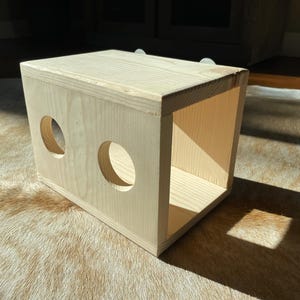 May include: A wooden box with two circular openings on the front. The box is made of light wood and has a natural finish.