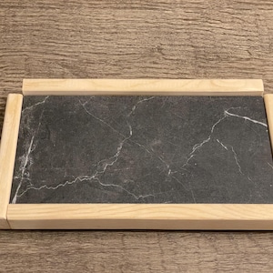 May include: A rectangular tray with a natural wood frame and a black marble insert. The tray is perfect for serving snacks or drinks.