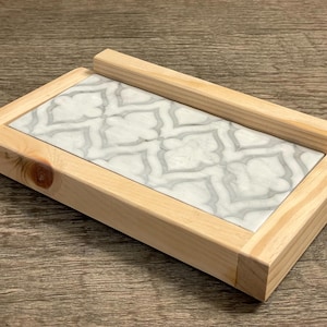 May include: A white marble soap dish with a geometric pattern, set in a natural wood frame.