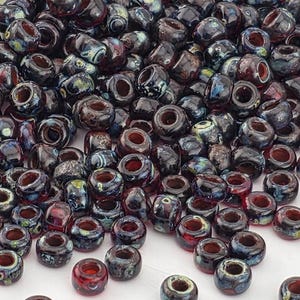 May include: A collection of dark, round glass beads with a hole through the center. The beads have a mix of colors, including dark blue, red, and hints of green and yellow. The beads are suitable for jewelry making and crafts.