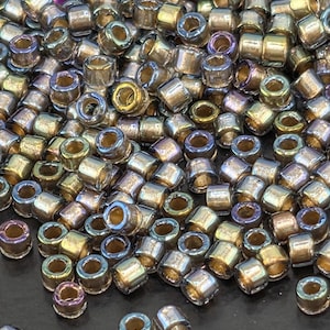 May include: Close-up of a pile of small, cylindrical beads with a metallic finish. The beads have a mix of colors, including gold, silver, and hints of iridescent hues. The beads are scattered, creating a textured surface.