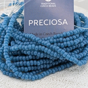 May include: A pile of blue PRECIOSA Czech beads. The beads are strung together and are a light blue color. The label reads "TRADITIONAL CZECH BEADS" and "PRECIOSA" with text that says "Made in Czech Republic".