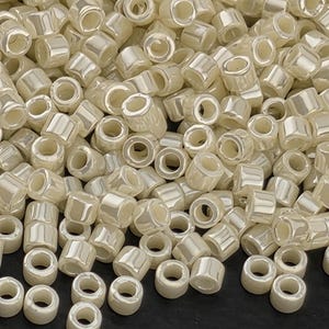 May include: A close-up shot of a pile of ivory-colored, cylindrical beads. Each bead has a hole running through the center, and a shiny, pearlescent finish. The beads are scattered, creating a textured surface.