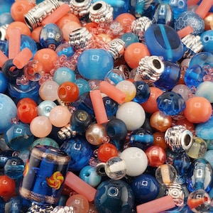 May include: A collection of assorted beads in shades of blue, orange, and pink. The beads vary in size and shape, including round, cylindrical, and decorative metal beads. Some beads have a marbled or textured appearance.