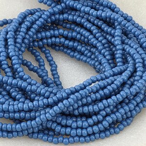 May include: A pile of small, round, blue glass beads. The beads are strung together, creating a textured, layered effect. The color is a muted, dusty blue, and the beads appear to be uniform in size and shape. Ideal for jewelry making and crafts.