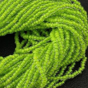 May include: Close-up of a pile of bright green seed beads. The beads are small, square-shaped, and strung together, creating a textured, organic appearance. The beads are a vibrant, solid green color, and the image is well-lit, highlighting the details of the beads.