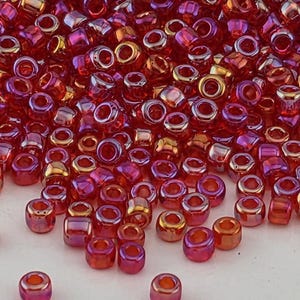 May include: A collection of small, cylindrical glass seed beads in a vibrant red hue with a metallic, iridescent finish. Each bead features a central hole and a smooth, reflective surface, creating a cluster of shiny, light-catching components.
