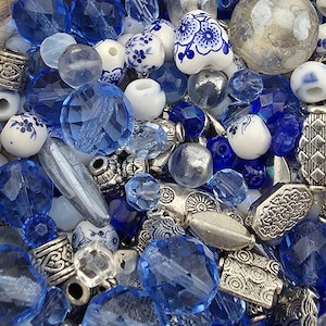 May include: A collection of blue beads, including faceted crystal, opaque, and ceramic beads with floral patterns. Silver-colored metal spacer beads are also present, creating a mix of textures and shapes. The beads are in various shades of blue and white.