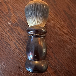 May include: A brown wooden shaving brush with a black handle and a white bristle brush head.