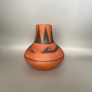May include: A terracotta vase with a black geometric design. The vase has a rounded body and a narrow neck.