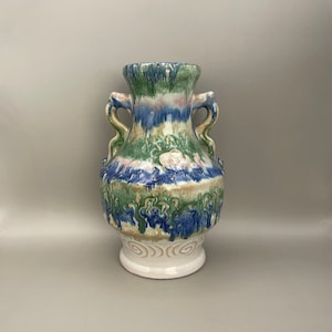 May include: A ceramic vase with a green, blue and pink glaze. The vase has two handles and a swirling pattern on the bottom.