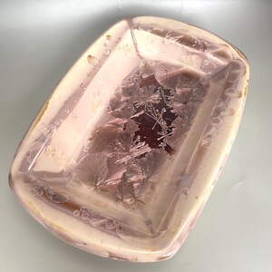 May include: A rectangular ceramic serving dish with a light pink and brown glaze. The dish features a unique crystalline pattern in the centre, with a raised rim and rounded corners. Ideal for serving appetizers or small dishes.