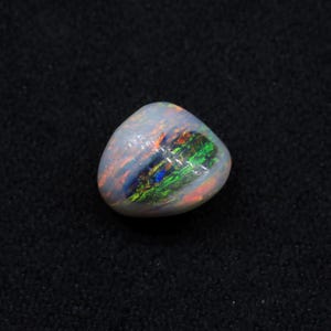 May include: A white opal gemstone with a green, blue, and orange iridescent sheen. The opal is a teardrop shape and is set against a black background.