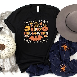 May include: Black t-shirt with a retro-style graphic that says "Hippy Halloween" with a peace sign, skull, pumpkin, bat, and eyes.
