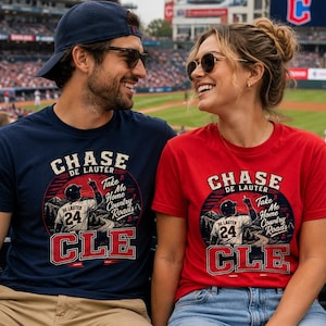 May include: A navy blue t-shirt and a red t-shirt with a graphic design featuring the text "CHASE DE LAUTER" and "Take Me Home Country Roads". The design includes a baseball player and the letters "CLE".