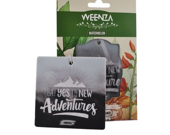 Puede incluir: Un ambientador de coche blanco con una escena de montaña en blanco y negro y el texto "Say yes to new adventures". El ambientador está empaquetado en una caja de cartón con un diseño floral y el texto "Weenza Watermelon".
