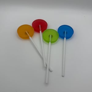May include: Four colorful lollipops with transparent, circular candy tops in yellow, red, green, and blue. Each lollipop has a white stick. The lollipops are arranged on a white background.