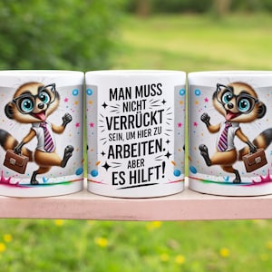 May include: White ceramic coffee mugs with a cartoon meerkat wearing glasses, a tie, and carrying a briefcase. The mugs have the text "MAN MUSS NICHT VERR&Uuml;CKT SEIN, UM HIER ZU ARBEITEN. ABER ES HILFT!" in black.