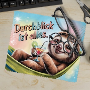 Op de afbeelding: Een microvezel schoonmaakdoek met een cartoon luiaard met een bril en een cocktail in een hangmat. De doek heeft de Duitse tekst "Durchblick ist alles". Een bril ligt op de doek.