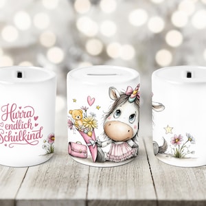 May include: White ceramic money bank featuring a cartoon unicorn with a pink dress, holding flowers and a teddy bear. The bank has a slot for coins and the text "Hurra endlich Schulkind" on one side. Decorative flowers and stars are also present.
