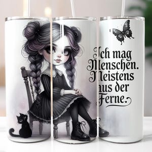 Könnte beinhalten: Weißer Becher mit einer gotischen Illustration eines Mädchens mit geflochtenen Haaren, das auf einem Stuhl sitzt, mit einer schwarzen Katze. Der Becher hat auch einen schwarzen Schmetterling und den deutschen Text: "Ich mag Menschen. Meistens aus der Ferne."