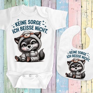 May include: White baby onesie and bib set featuring a cartoon wolf wearing a sheep hat. The onesie and bib have the text "KEINE SORGE ICH BEISSE NICHT." in blue. The wolf is gray, white, and black.