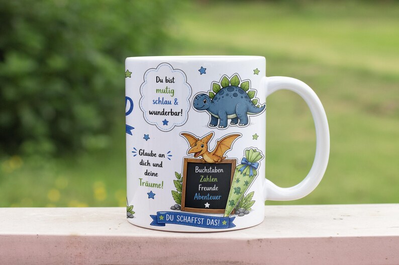 May include: White ceramic mug featuring cartoon dinosaurs and text in German. The mug has a blue Stegosaurus, a Pterodactyl, and a chalkboard with words. The mug also has text that says "Du bist mutig schlau & wunderbar!" and "DU SCHAFFST DAS!"