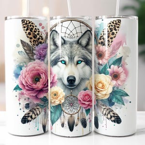 May include: White tumbler featuring a wolf with blue eyes, surrounded by flowers, feathers, and a dreamcatcher design. The design includes pink, purple, and yellow flowers, and a leopard print accent. The tumbler has a straw.