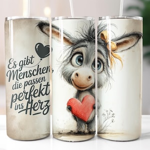 Könnte beinhalten: Ein Edelstahlbecher mit einem Cartoon-Esel, der ein rotes Herz hält. Der Esel hat große blaue Augen und eine gelbe Schleife. Der Becher trägt den deutschen Text "Es gibt Menschen, die passen perfekt ins Herz."