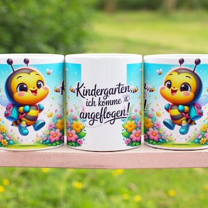 Könnte beinhalten: Drei weiße Keramikbecher mit einem fröhlichen Cartoon-Bienen-Design. Die Biene ist gelb und schwarz, mit Rucksack und Flügeln, vor einem blauen Himmel mit Blumen und Bienen. Der Text "Kindergarten, ich komme angeflogen!" ist ebenfalls vorhanden.