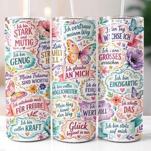 May include: Three cylindrical tumblers with straws featuring a white background decorated with colorful watercolor butterflies, flowers, and German motivational text including phrases like Ich bin stark und mutig and Ich glaube an mich.